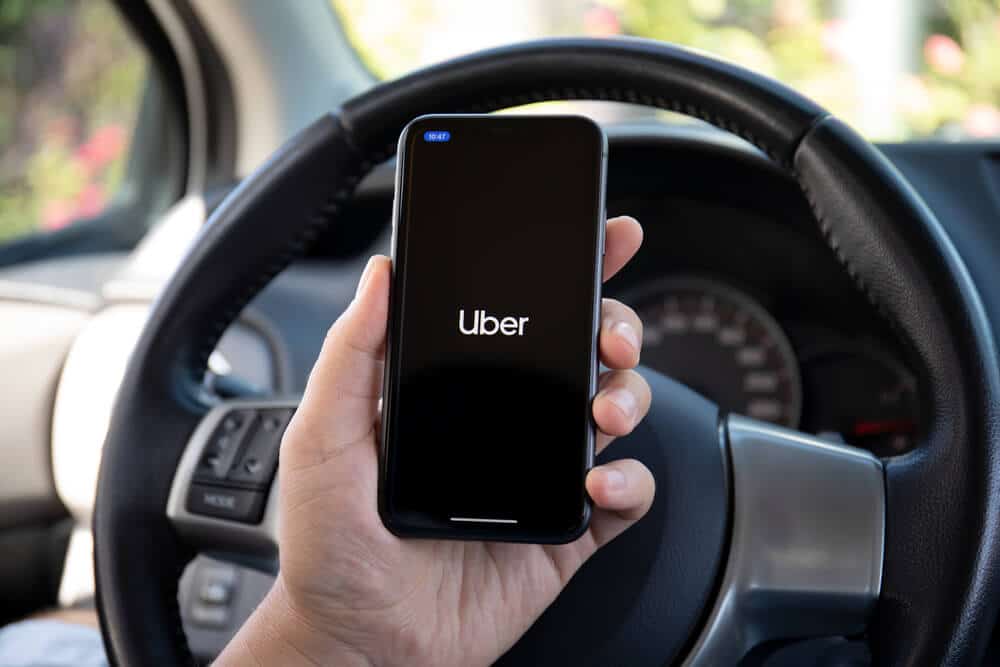 A person holding a phone while driving a car with the Uber app on it in Lisbon.