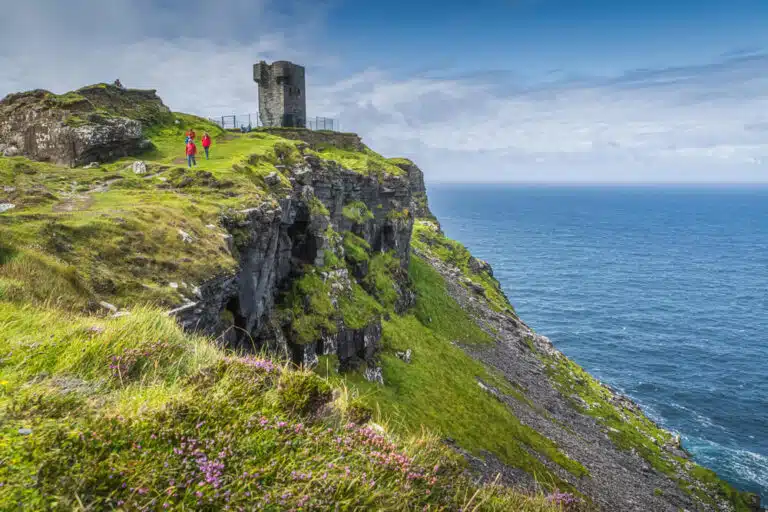 A man is standing on top of a cliff overlooking the ocean near the Cliffs of Moher, one of Ireland's most famous natural landmarks.